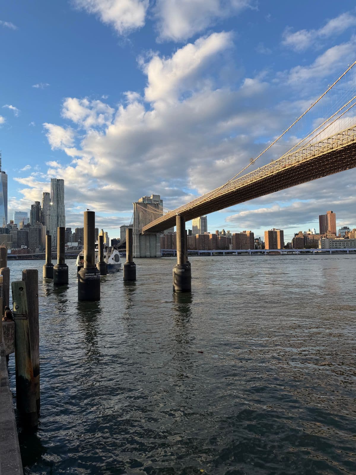 The Brooklyn Bridge from the East River waterfront with clouds and the downtown skyline