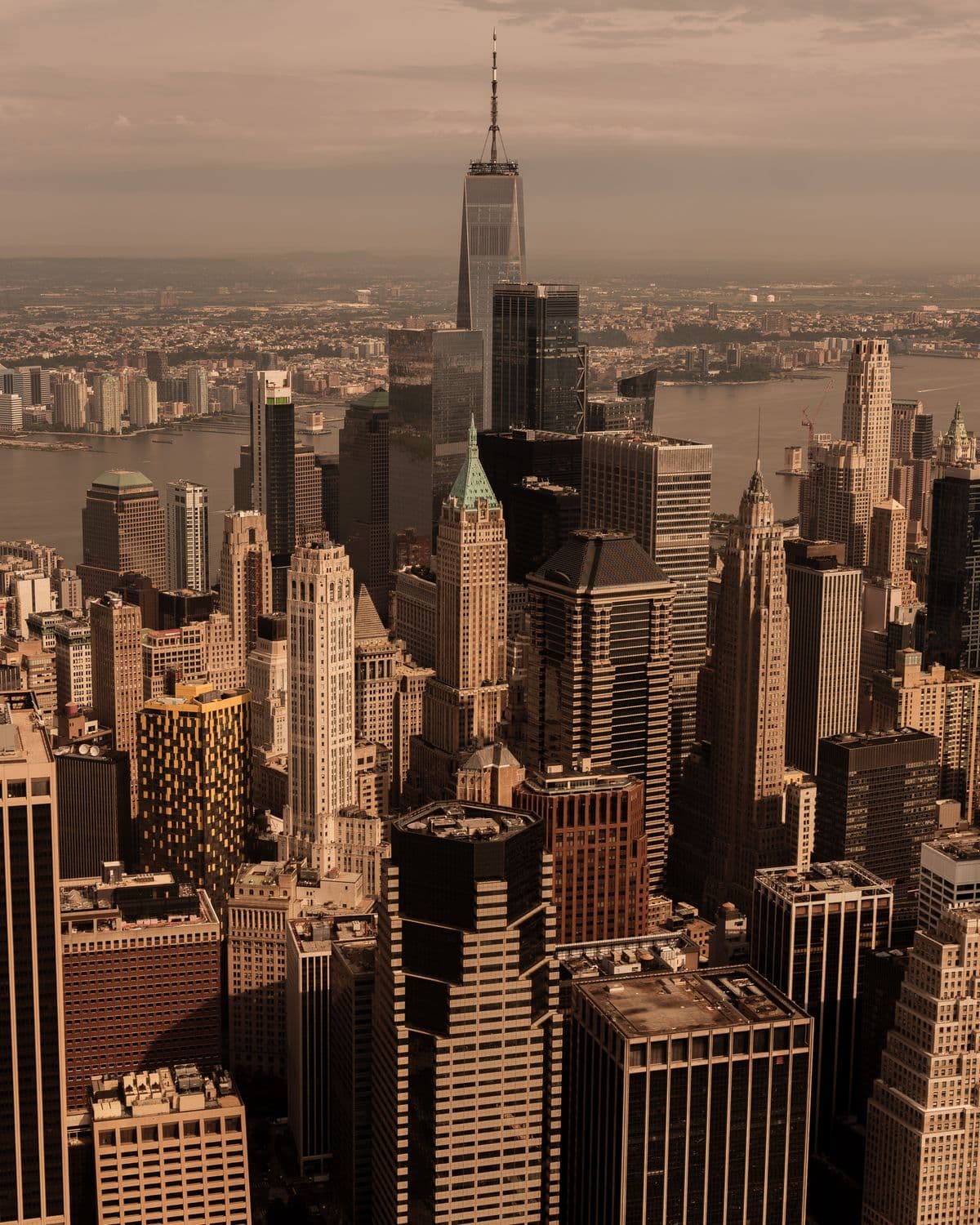 Aerial view of Lower Manhattan's skyscrapers at golden hour, One World Trade Center rising above the Hudson
