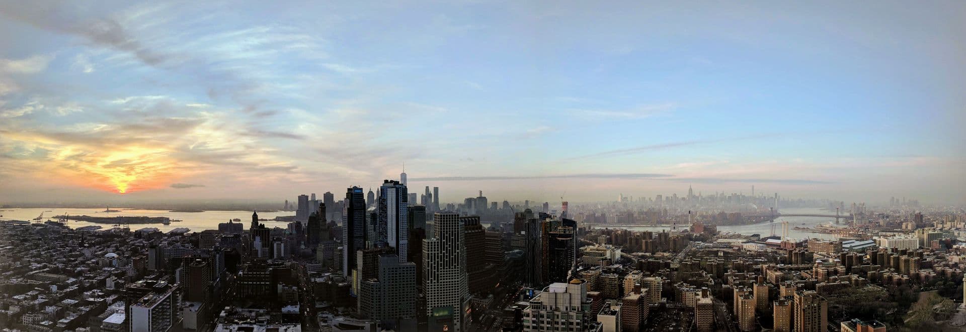 Wide panorama of the New York City skyline at sunset over the harbor and Brooklyn