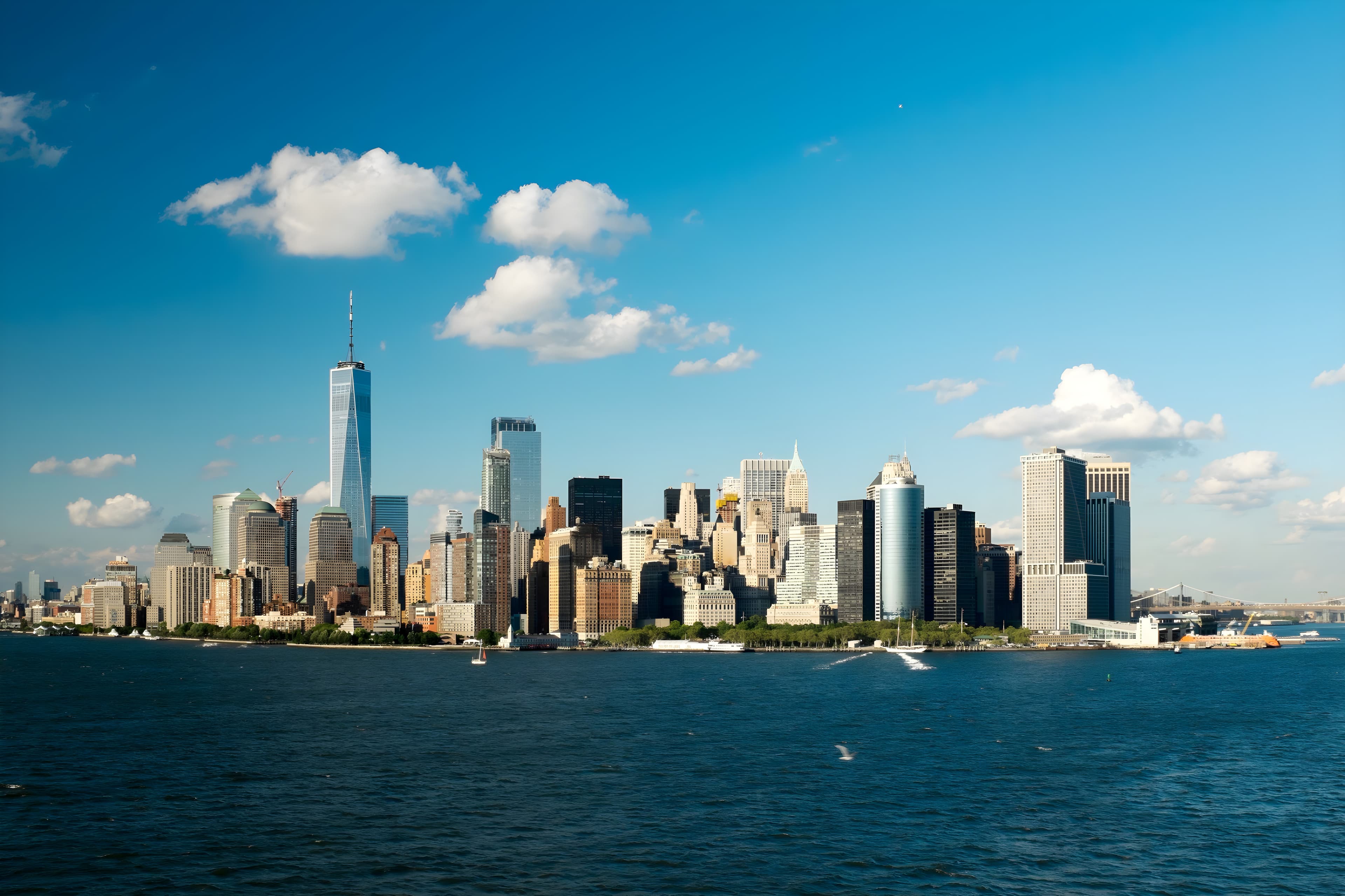 Lower Manhattan and One World Trade Center across the Hudson River beneath a blue sky with clouds